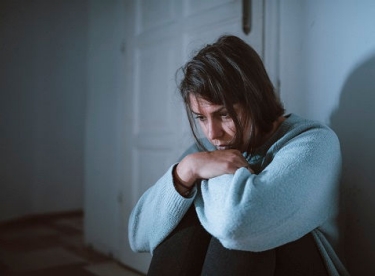 Woman sitting on the floor Young woman sits in her room in the dark, struggling with depression.