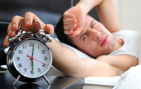 Man with sleep disorder reaches for alarm clock